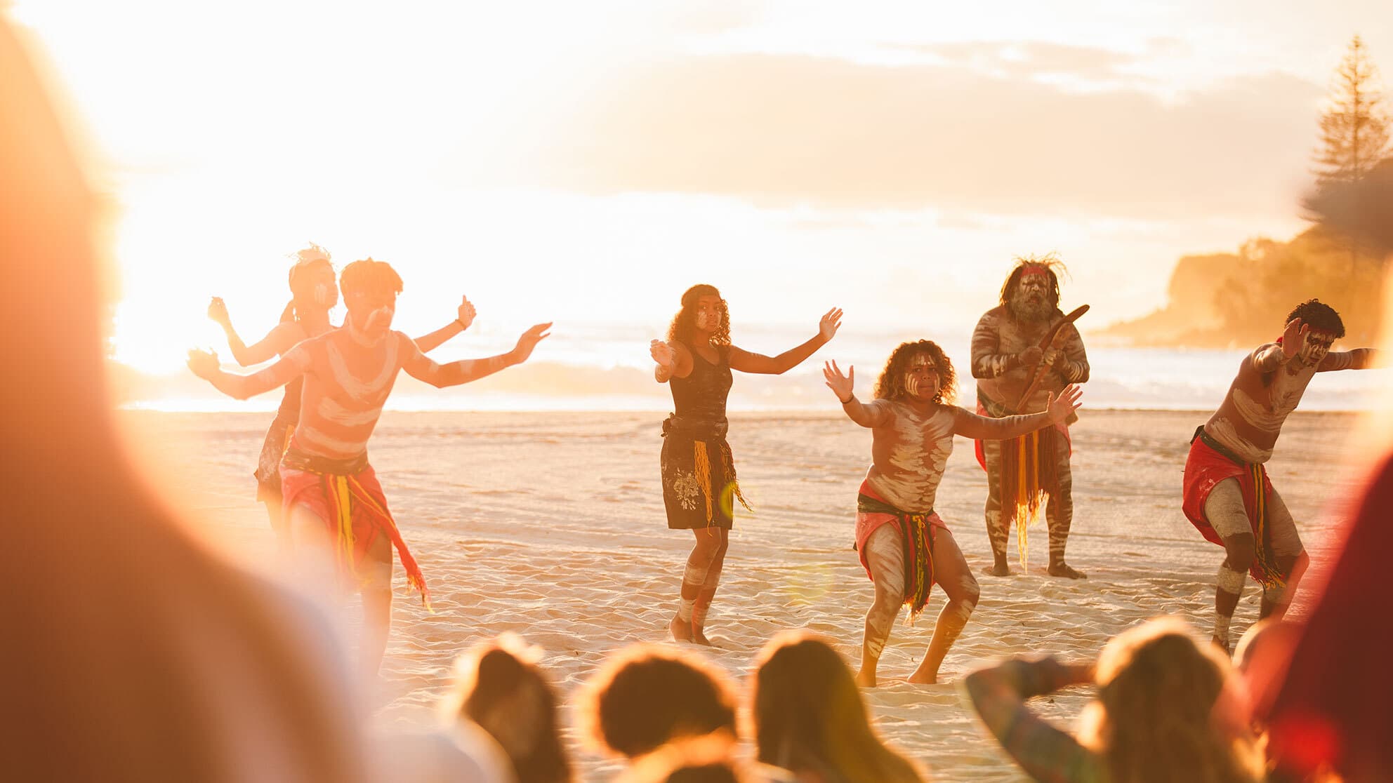Indigenous Australian people dance on the beach at sunrise.